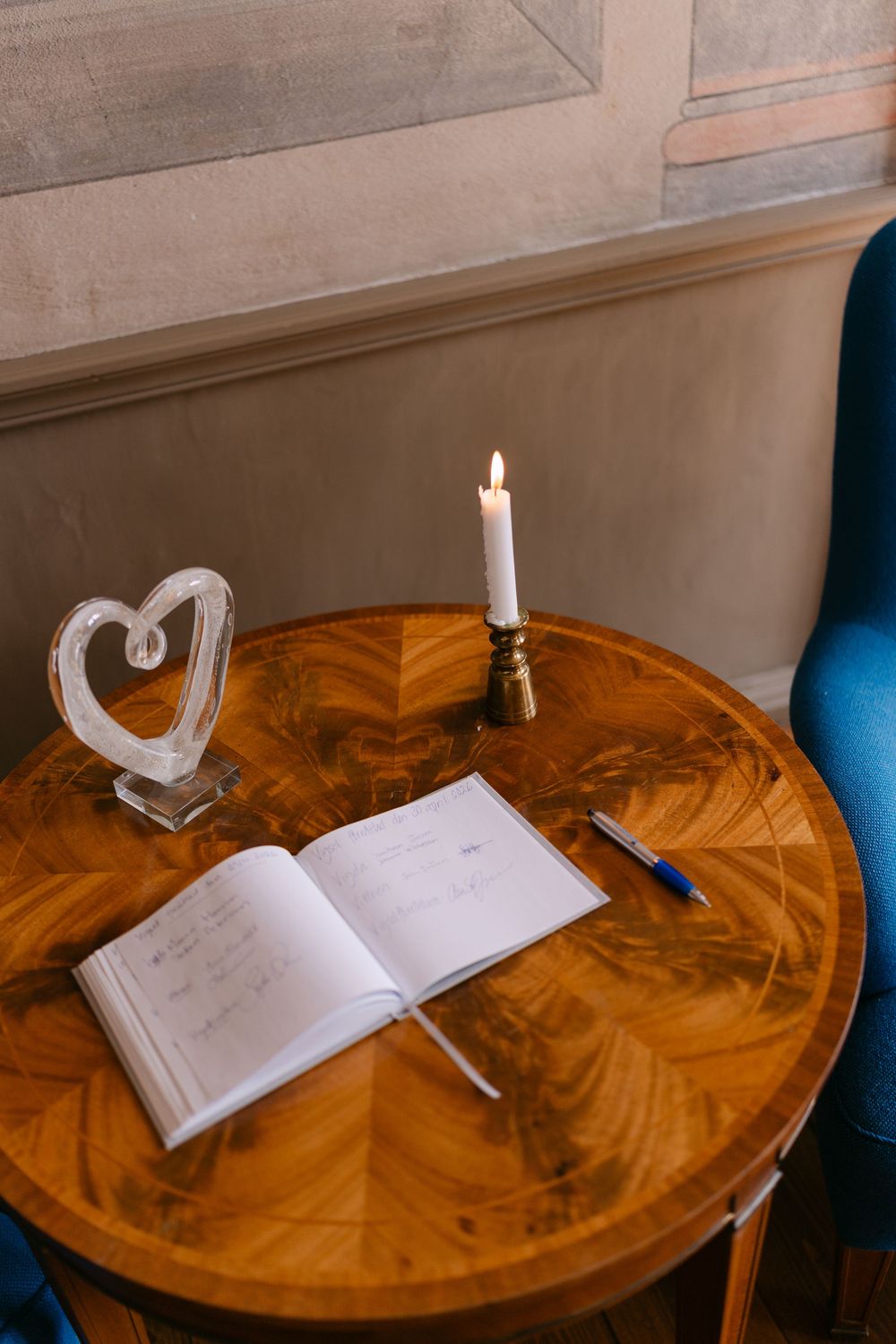 Elegant wedding guest book open on a wooden table with a lit candle, heart sculpture, and blue pen.  Borgerlig vigsel i Karlskrona.