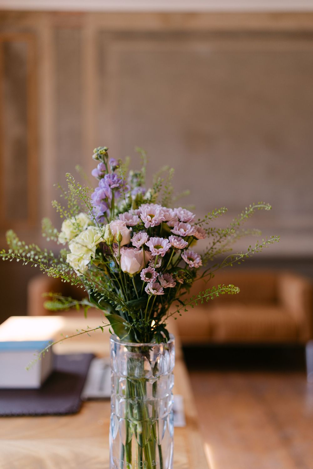 Glass vase with purple, pink, and white wildflowers on a wooden table. Borgerlig vigsel i Karlskrona på Nordenskjöldska gården.