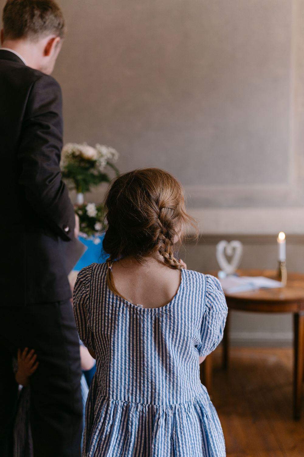 Young girl in blue striped dress and braided updo stands beside suited man at elegant wedding ceremony table. Borgerlig vigsel i Karlskrona
