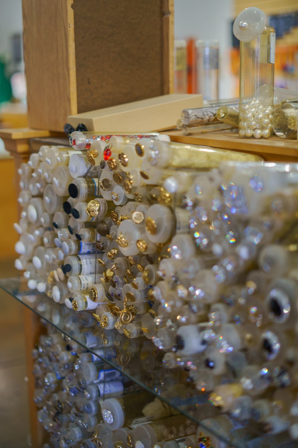 Display of decorative buttons and embellishments in white and gold tones, arranged on a retail counter in a craft store.