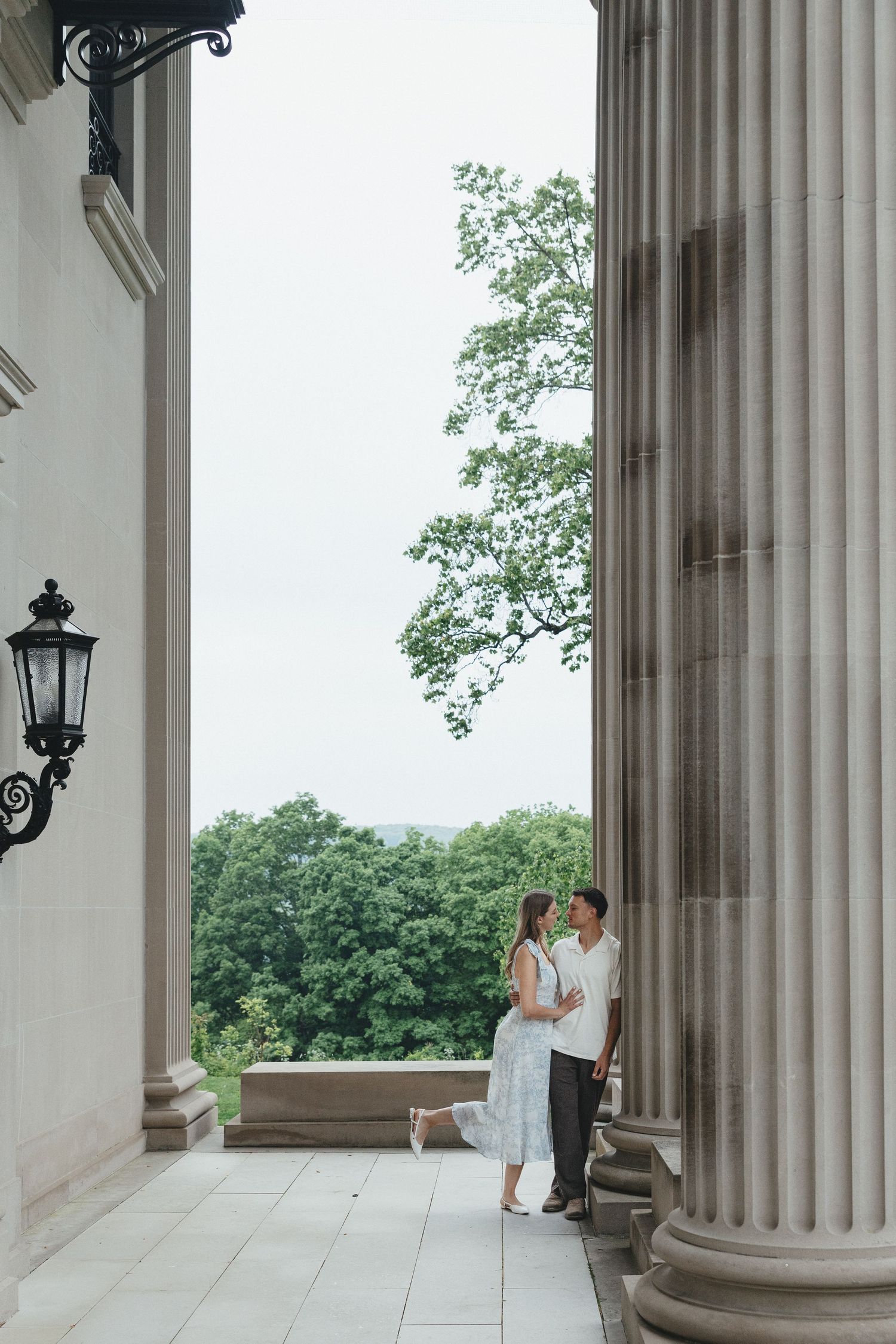 Couple holding hands walking along garden path toward ornate gate surrounded by lush greenery.