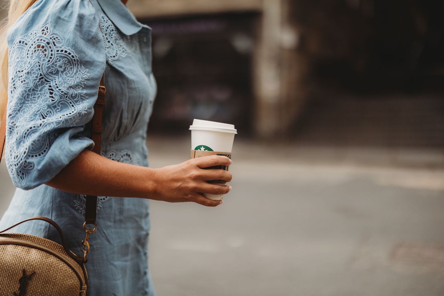 Woman in blue eyelet dress holding a Starbucks coffee cup outdoors on a city street.