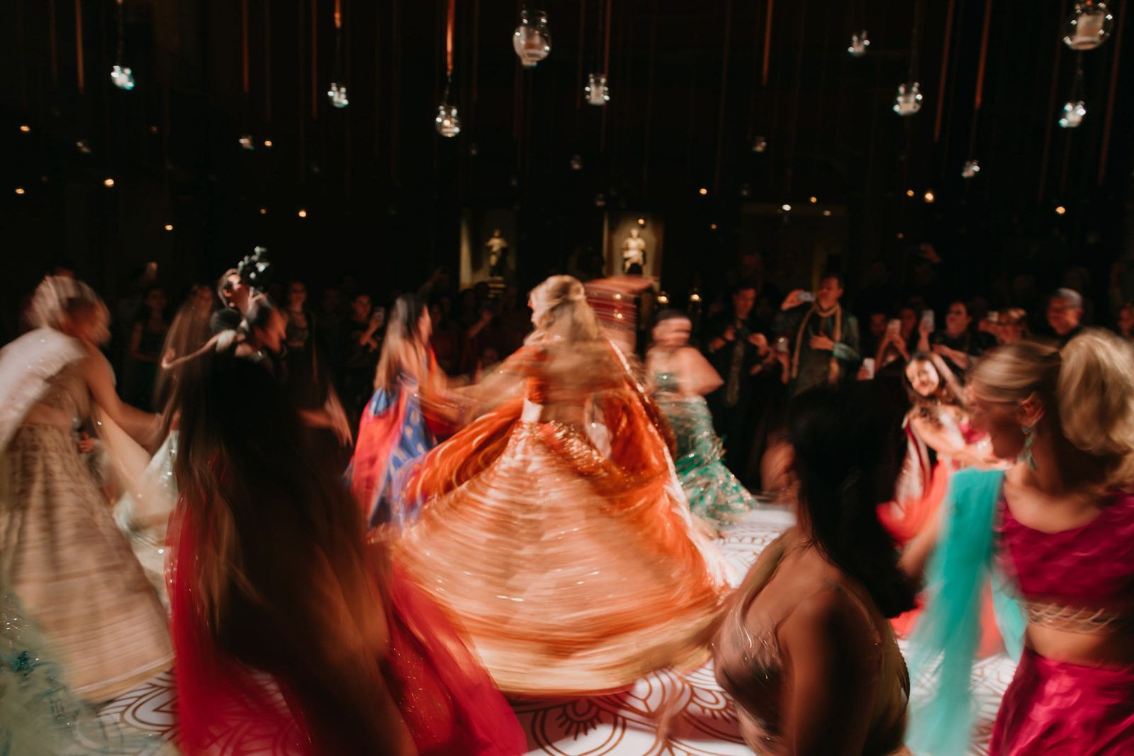 Colorful traditional Indian wedding dance with guests in vibrant lehengas twirling on a decorated dance floor.