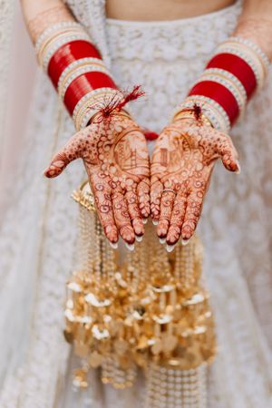 Close-up of traditional bridal hands with red bangles and intricate mehndi designs holding golden kalire.
