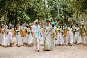 Wedding party members in white and turquoise attire pose together in an outdoor garden setting.