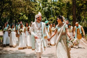 Large wedding party poses outdoors in coordinated white and turquoise outfits.