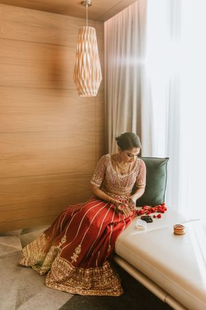 Traditional Indian bridal attire with red and gold lehenga photographed in elegant indoor setting.