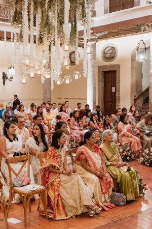 Guests seated in rows at an elegant indoor wedding ceremony with hanging floral and lantern decorations.