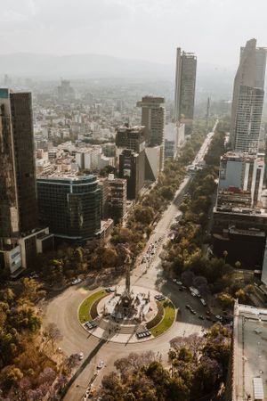 Aerial view of Mexico City's iconic Angel of Independence monument surrounded by modern skyscrapers and urban landscape.