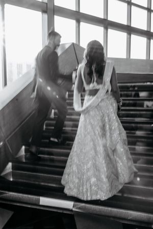 Black and white photo of a couple ascending stairs with dramatic window lighting.
