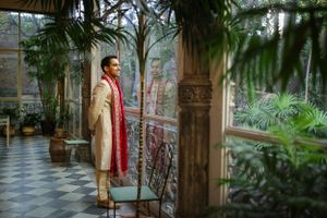 Person wearing traditional Indian attire stands in an elegant conservatory with ornate architecture.