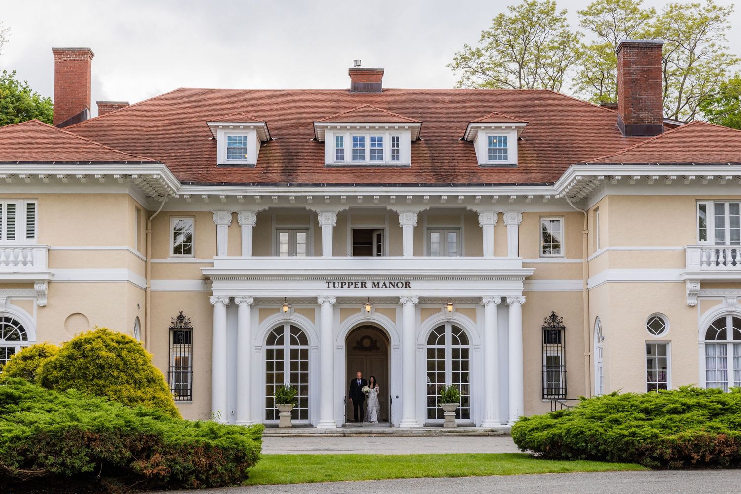 Elegant Tupper Manor estate with white columns, red roof, and lush greenery, perfect for weddings and events.