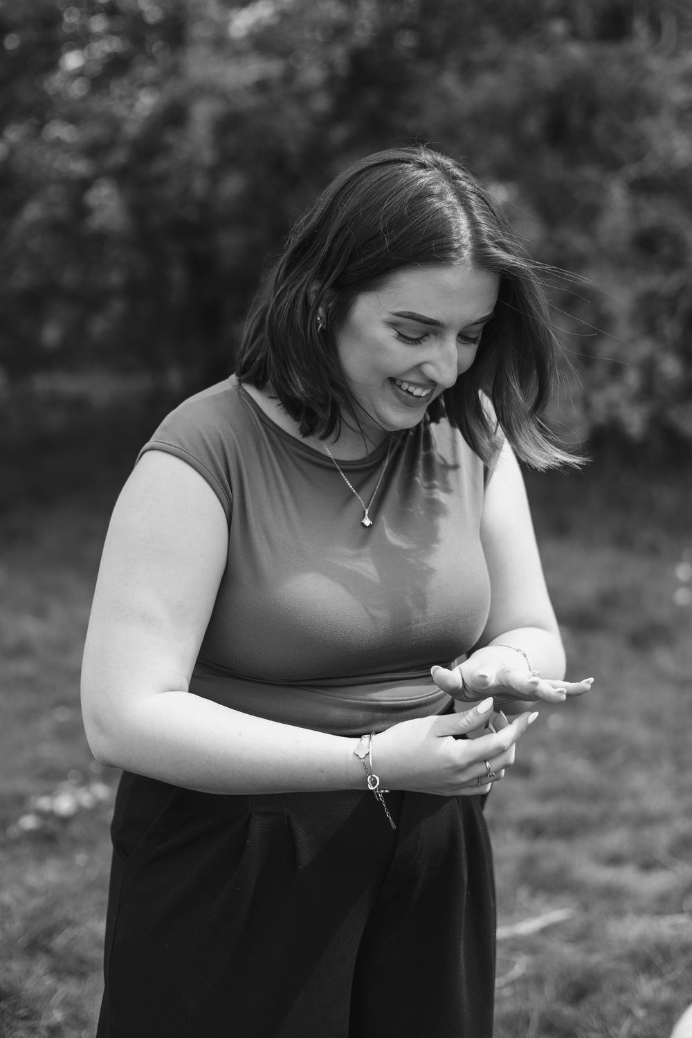 Black and white portrait of a young woman smiling while using her smartphone outdoors in a park.