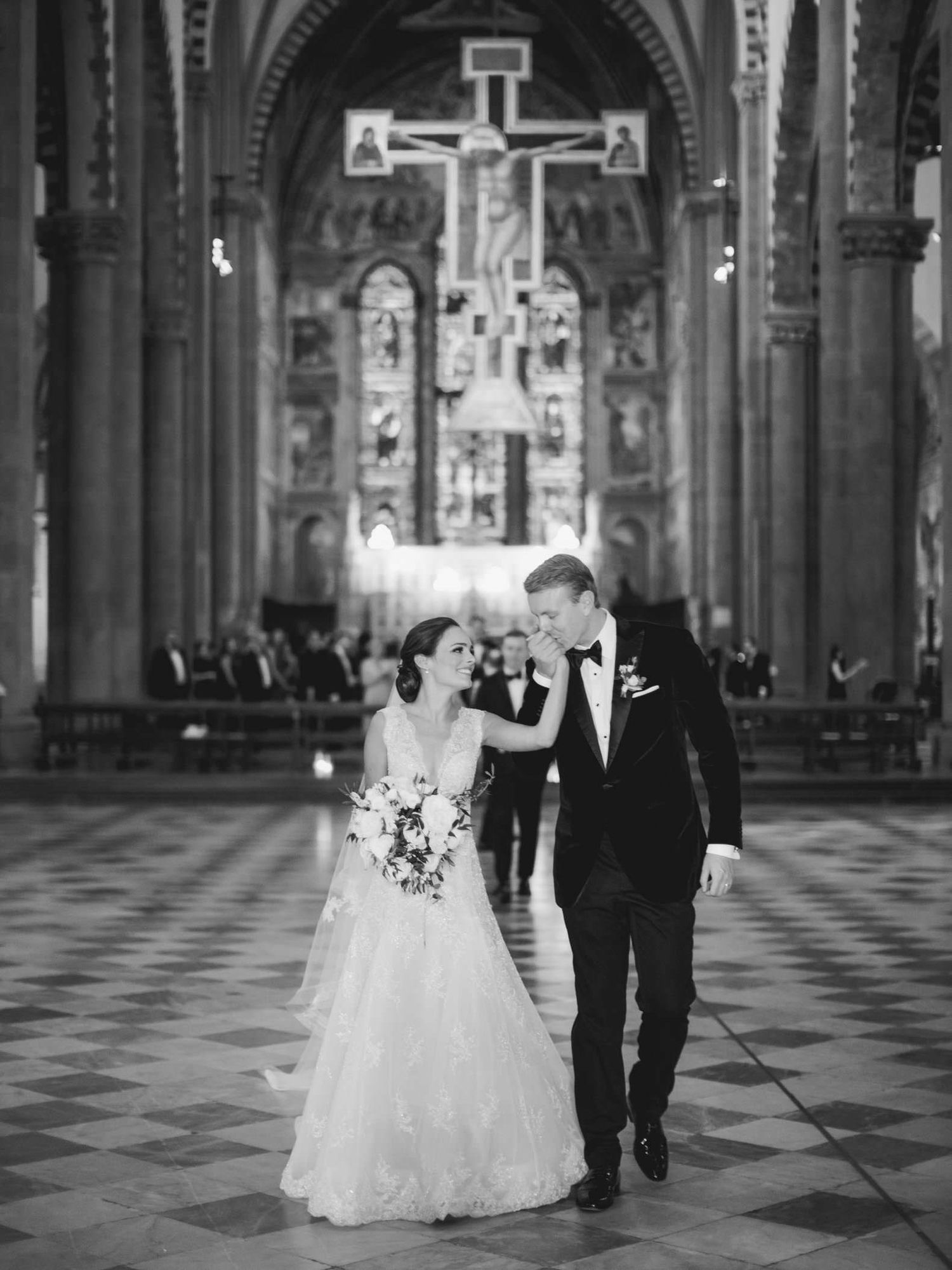 Black and white photo of a bride and groom walking down the aisle of an ornate church after their wedding ceremony.