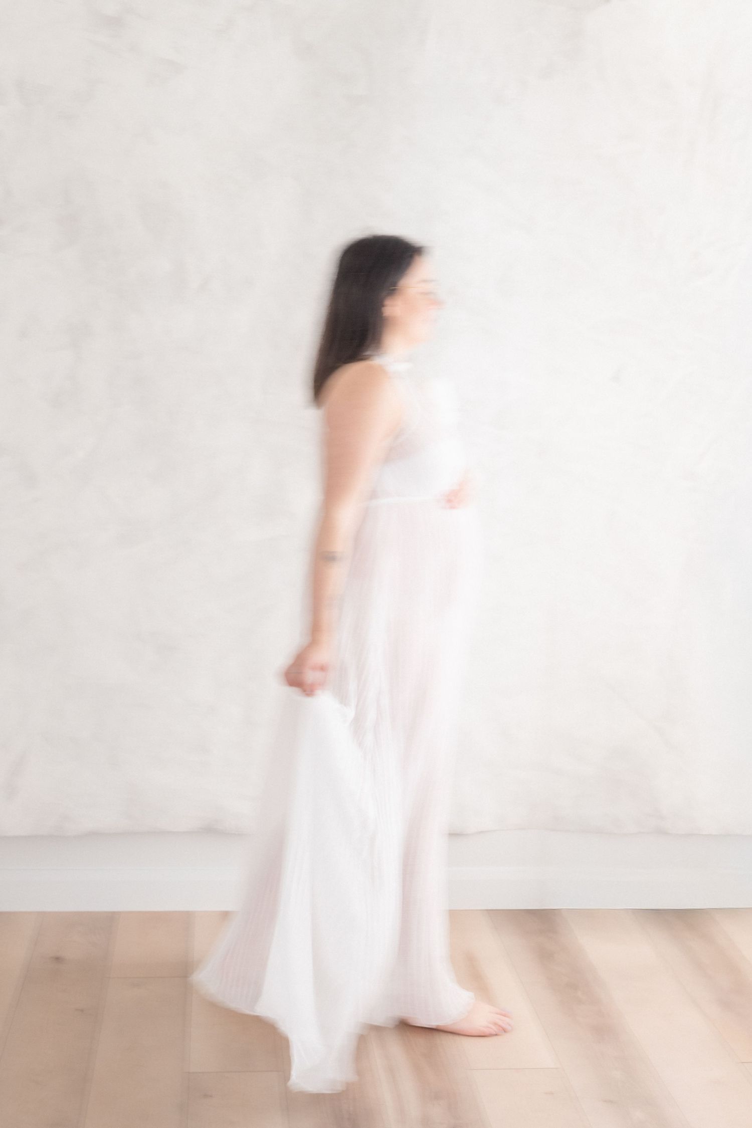 portrait fine art avec effet de mouvement fluide d'une future maman dans une robe vaporeuse de voilage blanc