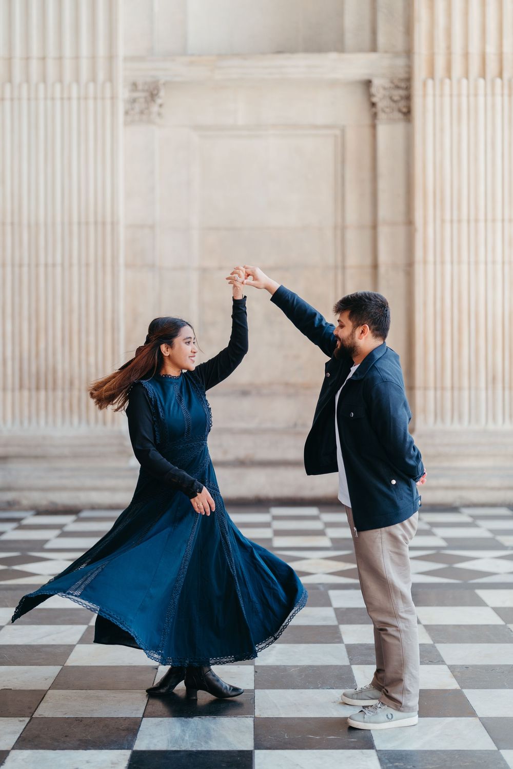 Couple dancing on checkered floor, woman in blue dress spinning, man in black jacket holding her hand up.