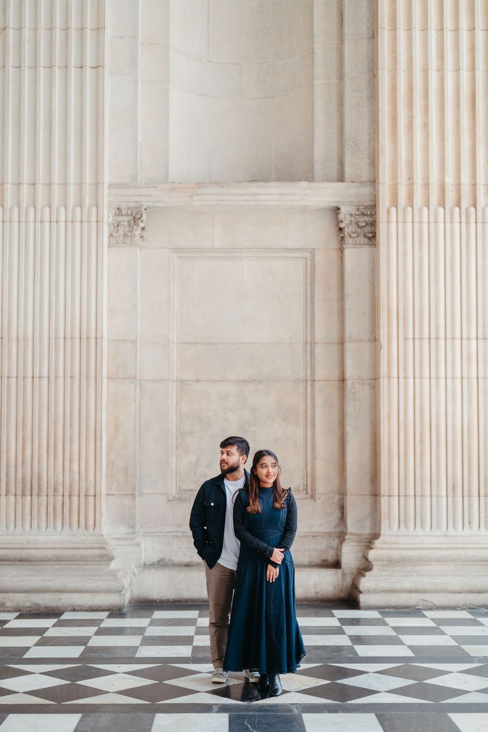 Couple posing in front of grand classical stone columns on a checkered marble floor.