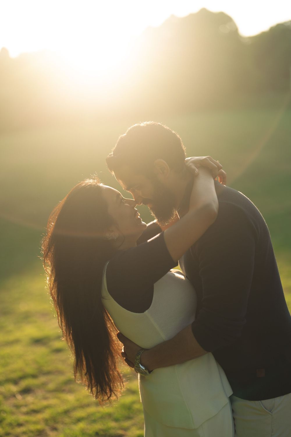 Couple sharing a romantic kiss at golden hour in a sunlit green field.