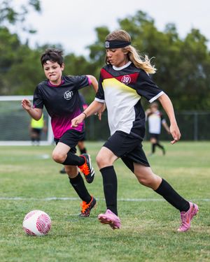 Two youth soccer players compete for the ball during a match on a green grass field, wearing black uniforms.