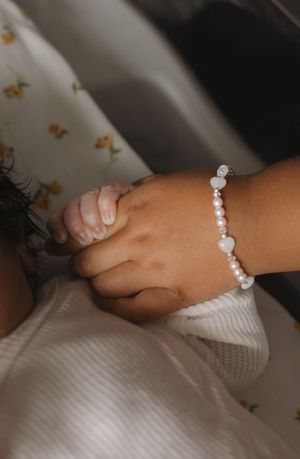Close-up of toddler hand wearing pearl heart bracelet gently holding newborn baby's tiny hand.