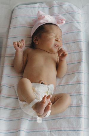 Newborn baby girl in pink bow headband lying on striped hospital blanket after delivery.