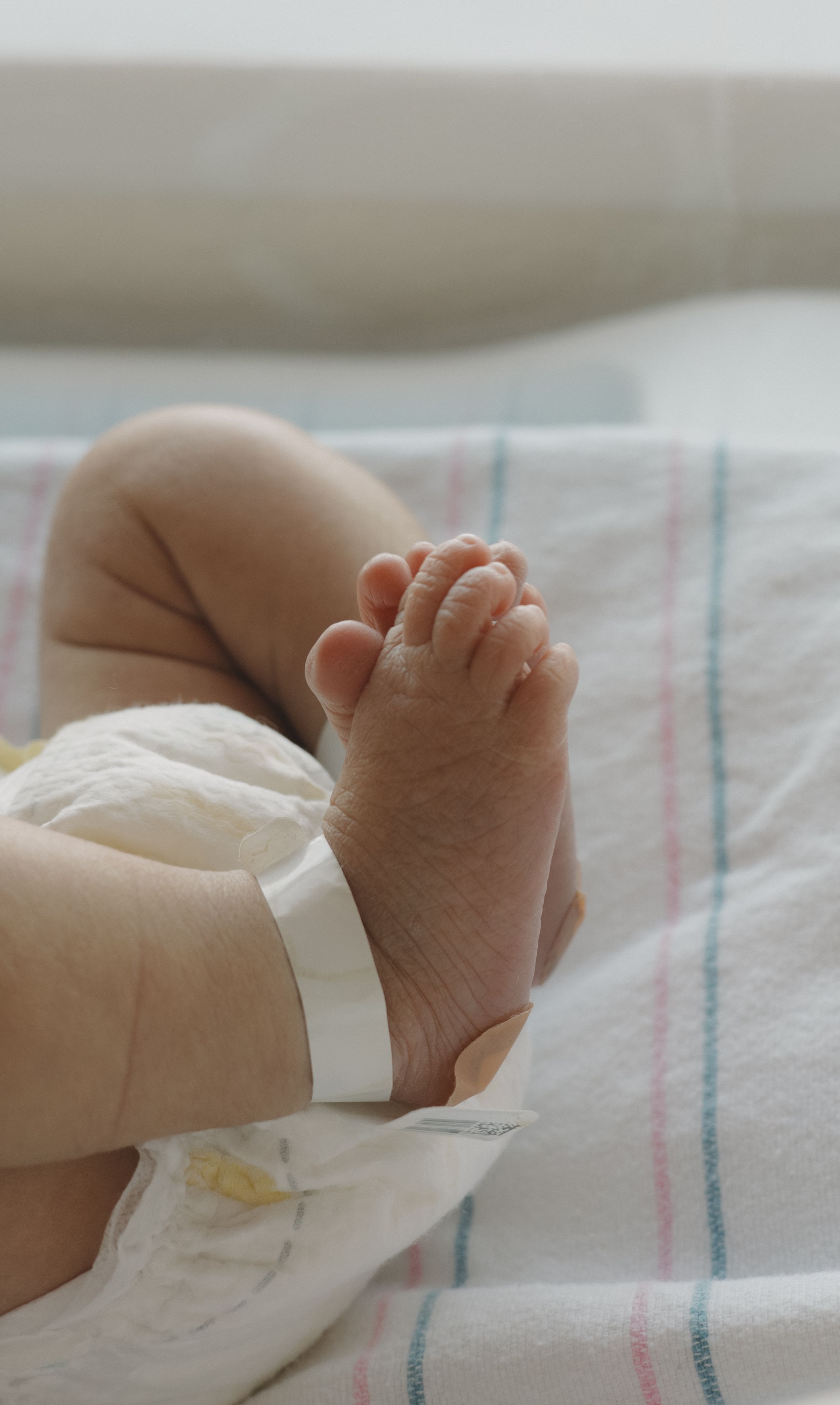 Close-up of tiny newborn baby feet with hospital ID bracelet on a striped blanket.