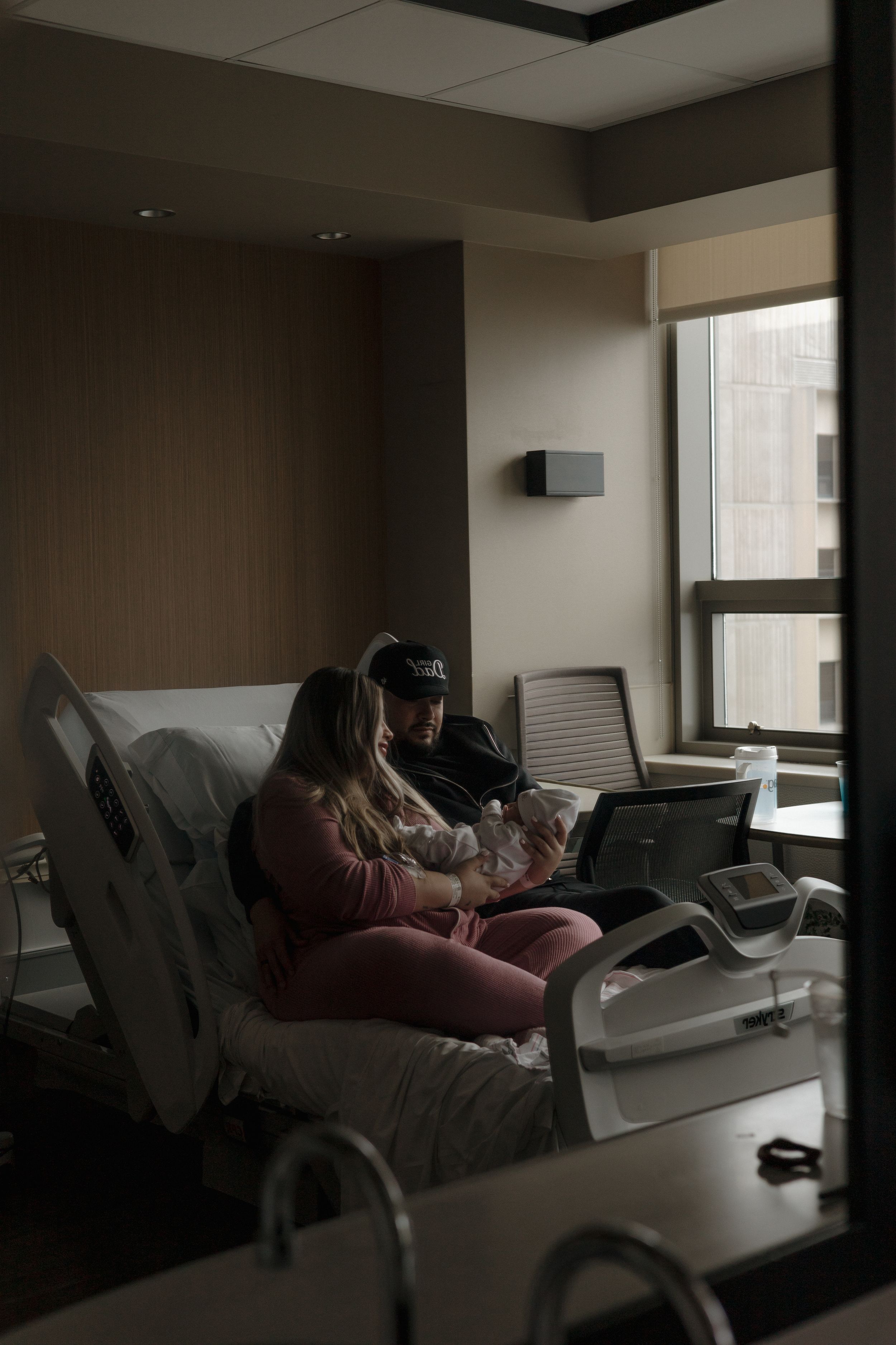 New family rests together in a dimly lit hospital room after welcoming their newborn baby.