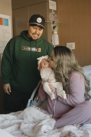New parents sharing tender moment with newborn baby girl in hospital room after birth.