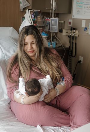 New mother in pink outfit lovingly holds her newborn baby in a hospital room after birth.