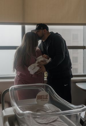 New parents share a kiss while holding their newborn baby in a hospital delivery room.