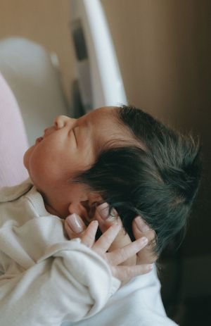 Close-up of a peaceful sleeping newborn baby with dark hair being cradled after birth.