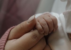Close-up of a newborn baby's tiny hand gently grasping a parent's finger after birth.