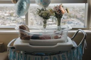 Newborn baby sleeping in clear hospital bassinet decorated with blue banner, balloons, and flowers.