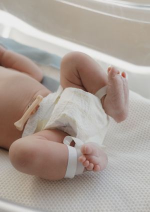 Close-up of newborn baby legs and feet in diaper with hospital ID bracelet in bassinet.