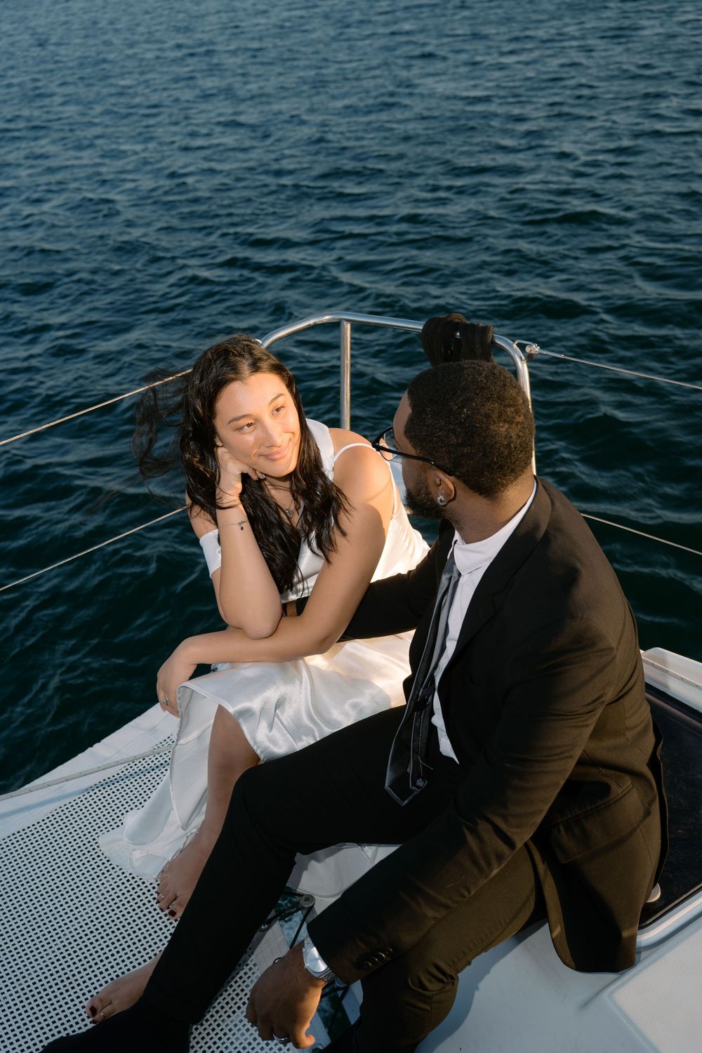 Bride and groom sitting intimately on a yacht deck overlooking deep blue ocean waters at sunset.