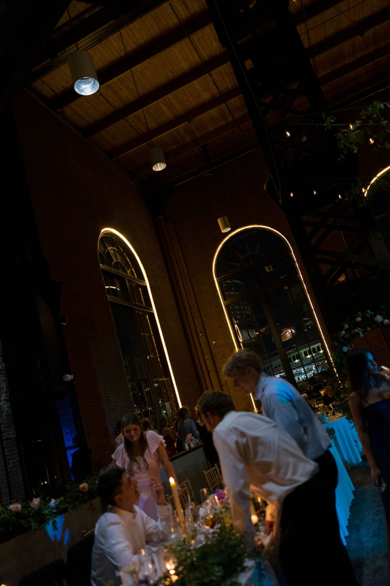 Dimly lit wedding reception venue with arched windows and candlelit tables during evening celebration.