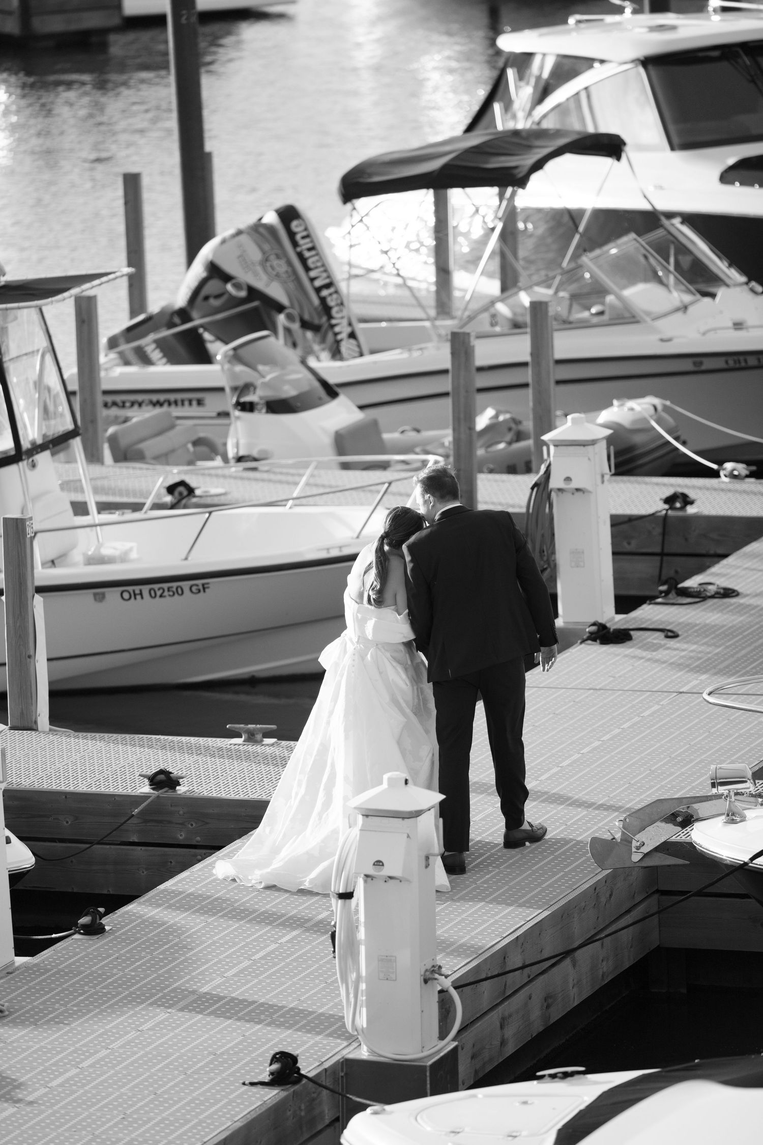 Bride and groom kissing on a boat dock surrounded by yachts in black and white.