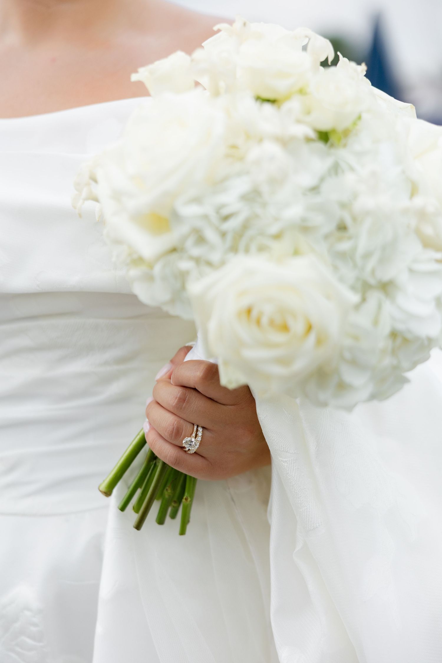 Bride holding a classic white rose bouquet with a diamond engagement ring on her hand.