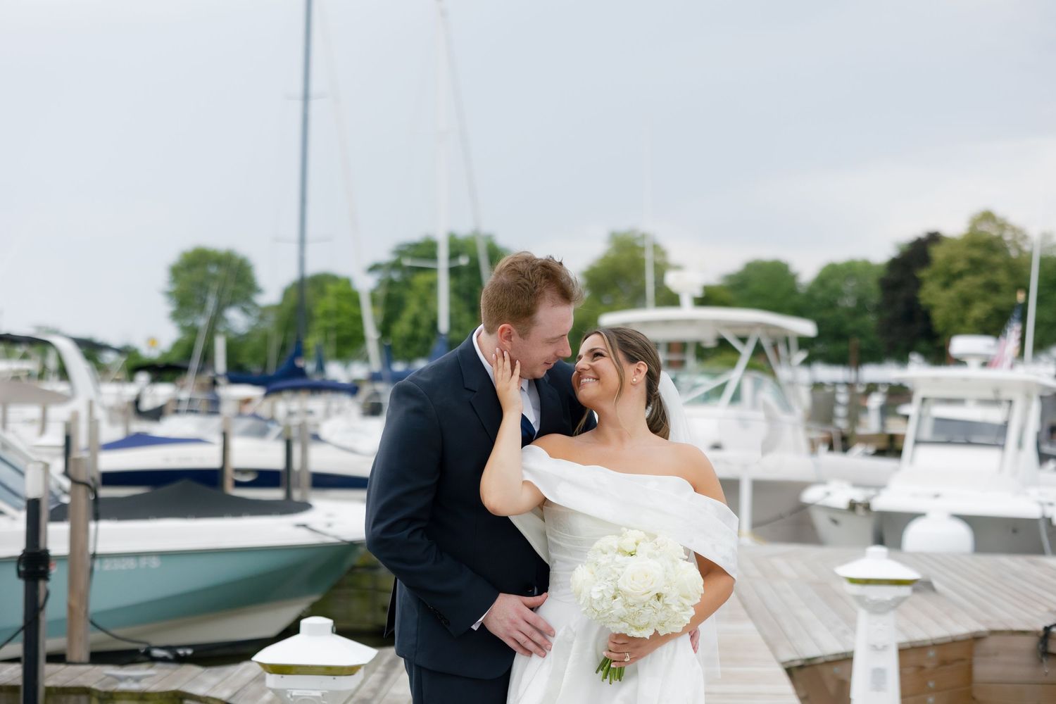 Bride and groom sharing a romantic moment on a marina dock surrounded by sailboats.