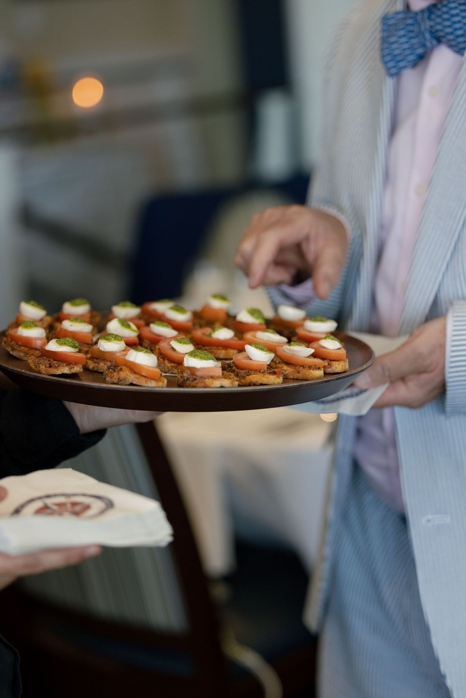 Server in bow tie presenting a tray of elegant caprese appetizers at a wedding reception.