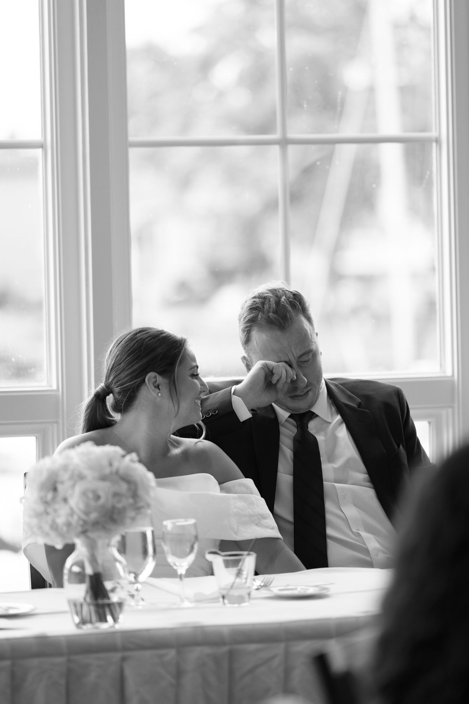 Black and white photo of bride and groom sharing an intimate moment at wedding reception table.