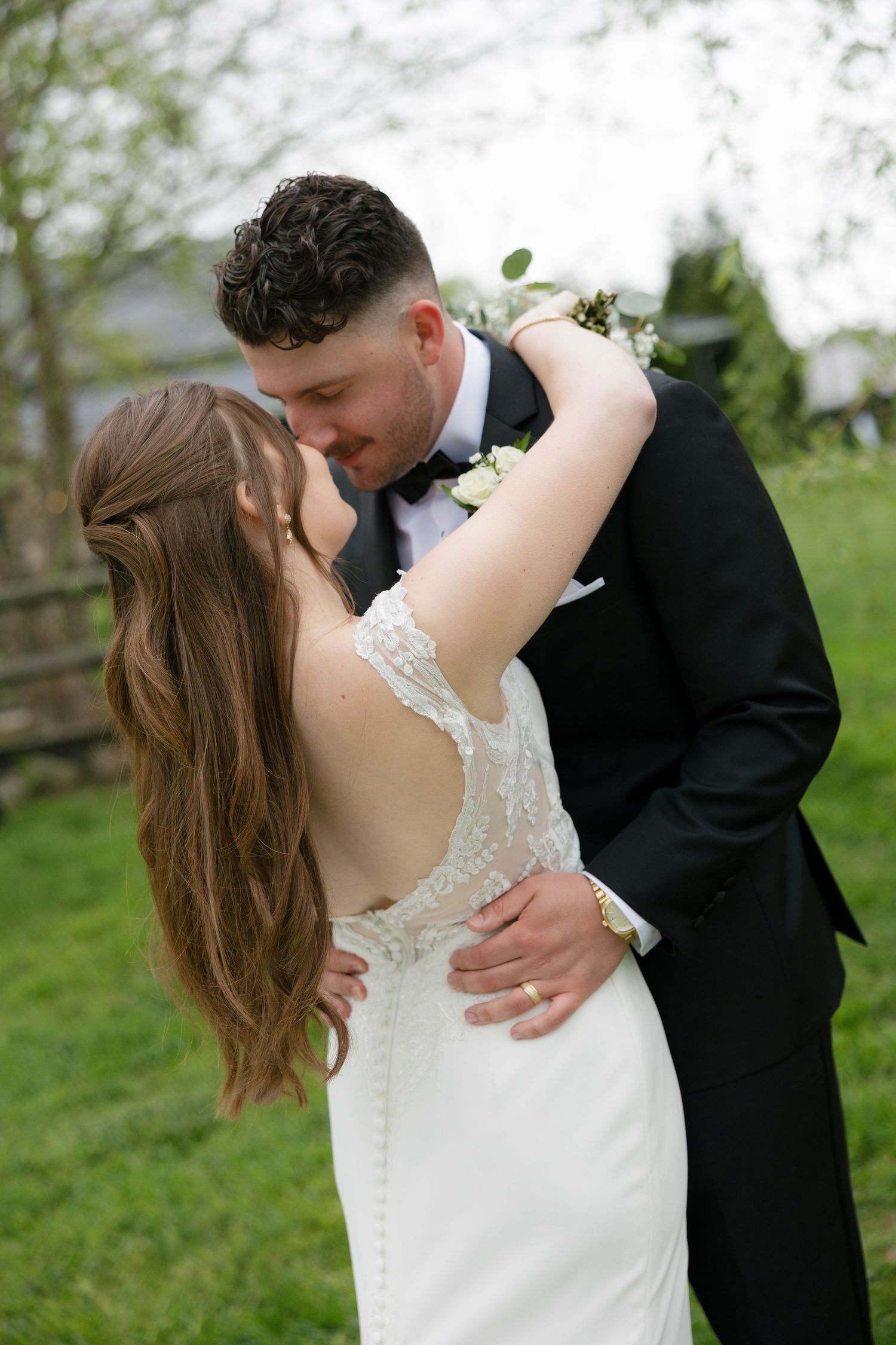 Bride and groom sharing a romantic embrace and kiss in a lush green outdoor setting.