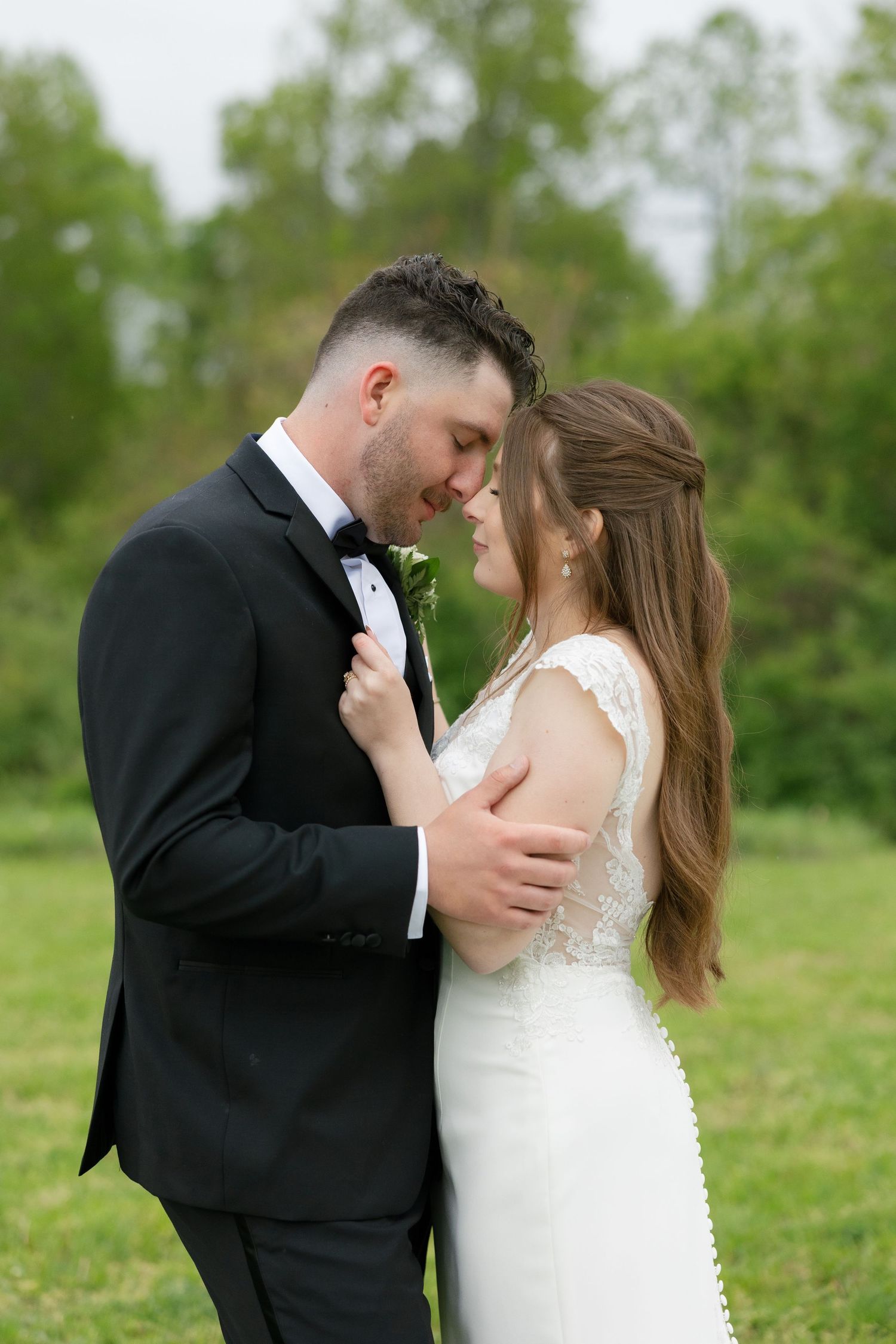 Bride and groom sharing an intimate forehead-to-forehead moment in a green outdoor setting.