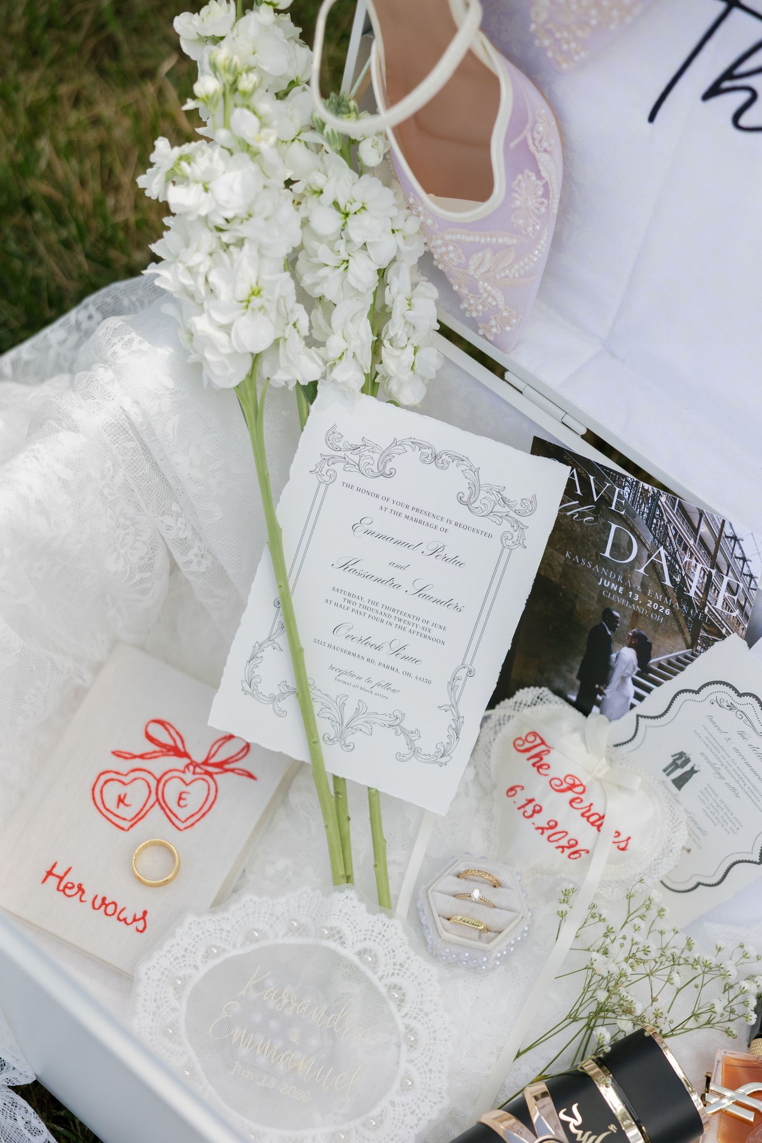 Flat lay of wedding details including vows booklets, rings, invitation, and white floral stems.