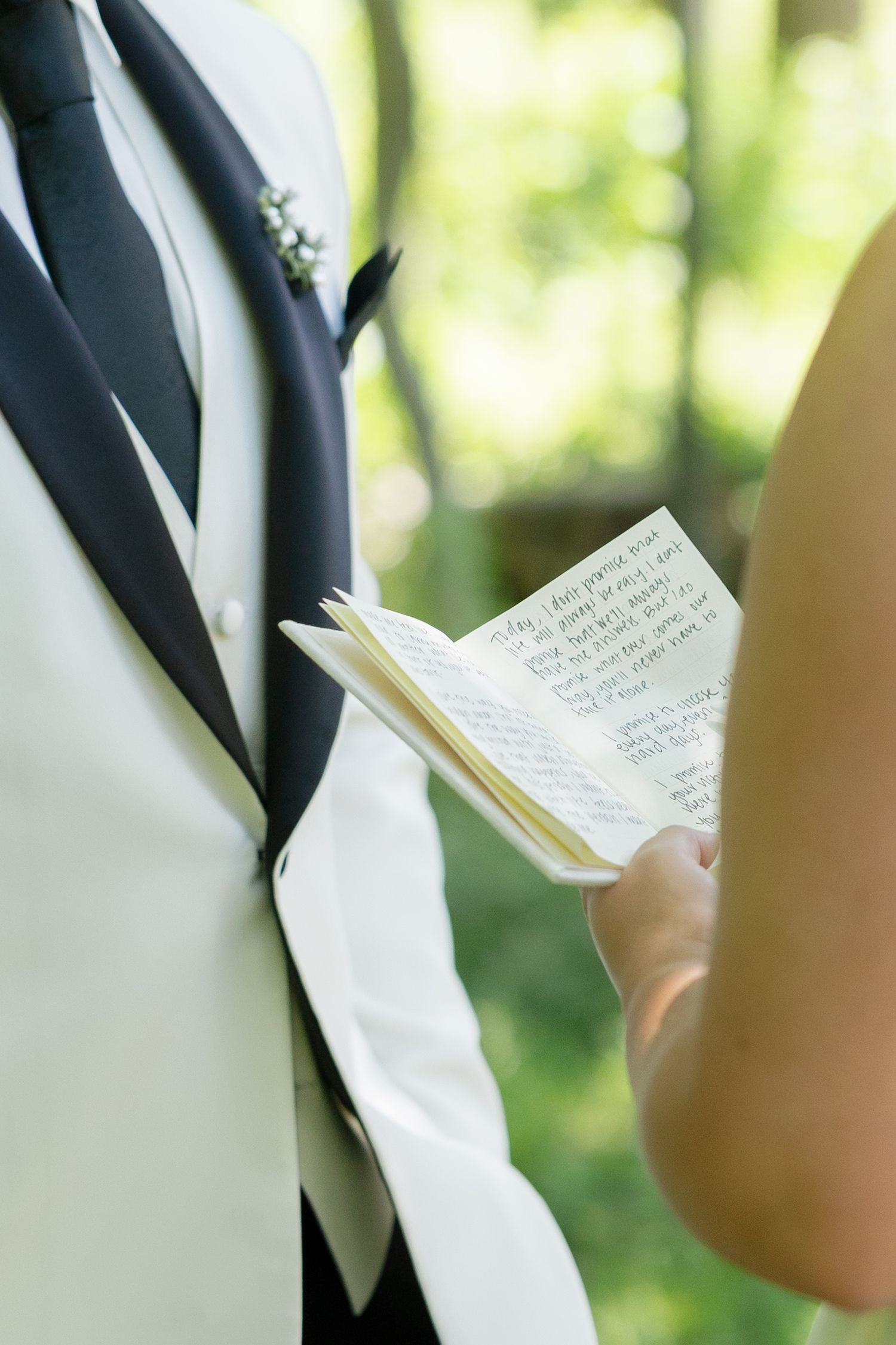 Close-up of handwritten wedding vows in small notebook held during outdoor forest ceremony.