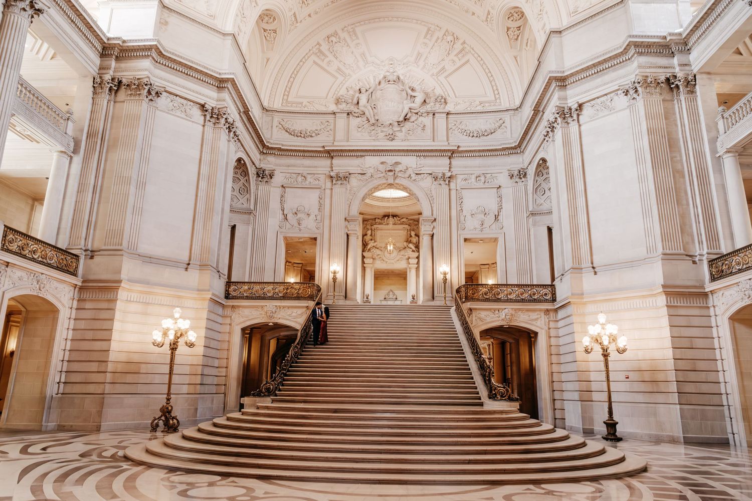 Grand marble staircase inside San Francisco City Hall with ornate Beaux-Arts architecture and elegant lamp posts.