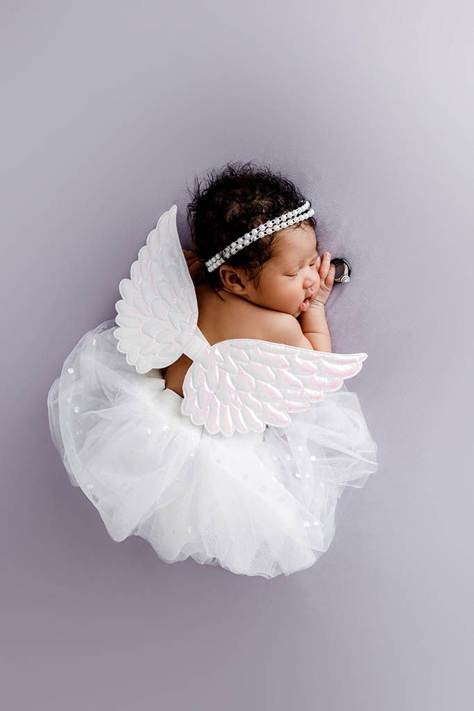 Sleeping newborn baby dressed in white angel wings and tutu on a gray background.