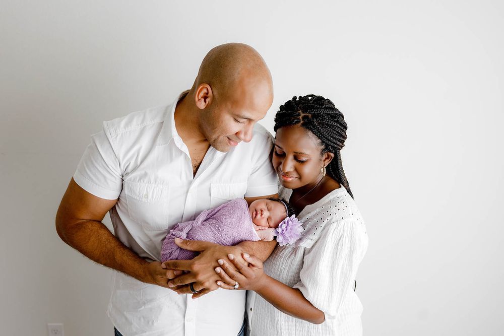 Happy parents holding their swaddled newborn baby in a bright white studio photography session by Perris newborn photographer.
