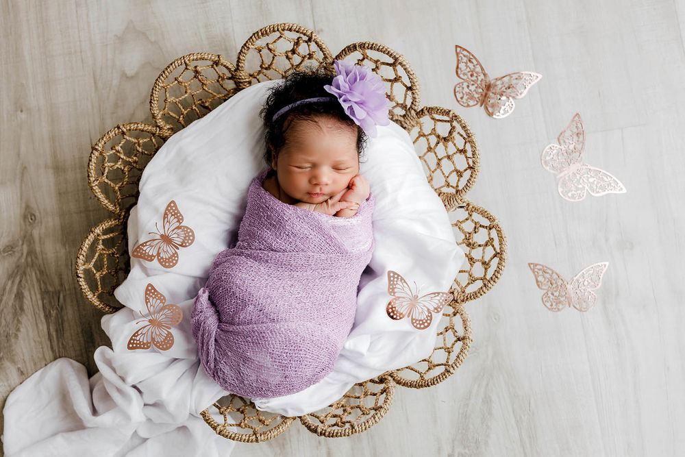 Sleeping newborn baby swaddled in purple wrap with butterfly decorations by Perris newborn photographer.