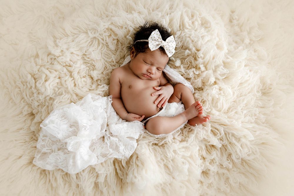 Sleeping newborn baby girl in white lace wrap and bow headband by Perris newborn photographer.